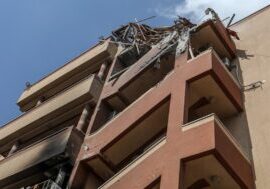Damaged multi-story building with debris hanging from upper floors.